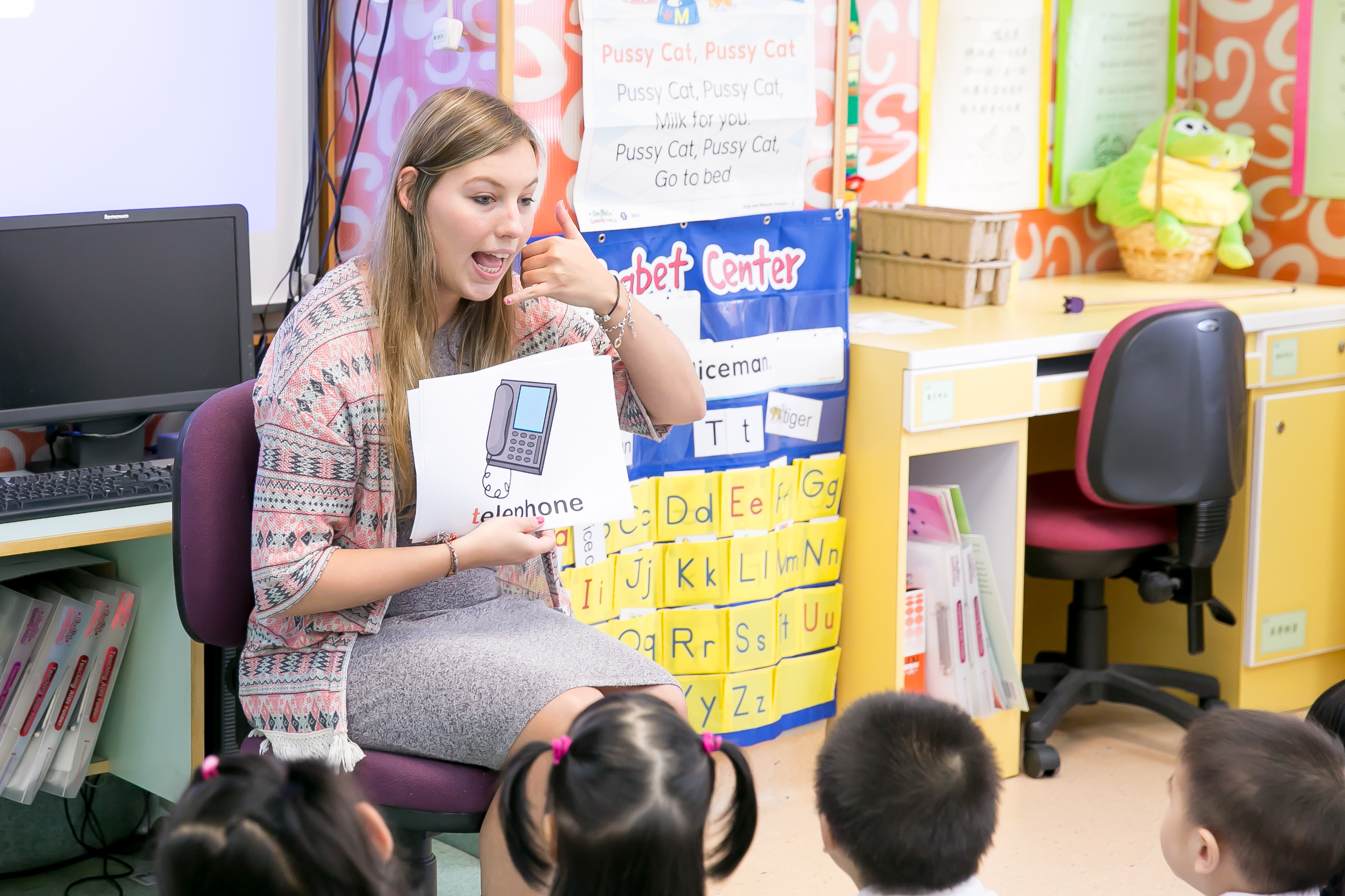 a female TEFL teacher is miming telephone picture to a group of asian children